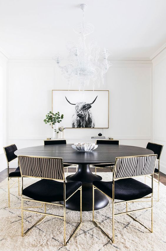 an elegant dining room with black furniture with gold frames, a printed rug and a statement chandelier and an artwork