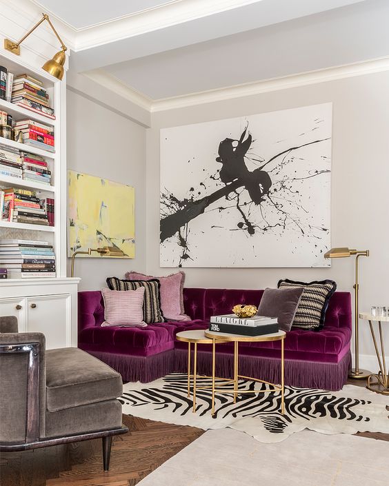 a refined and bold living room with a purple sectional as a centerpiece, a graphic artwork, a built-in bookcase and layered rugs