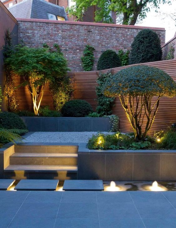a stylish minimalist backyard with built-in lights and lit up trees that are highlighted with these lights