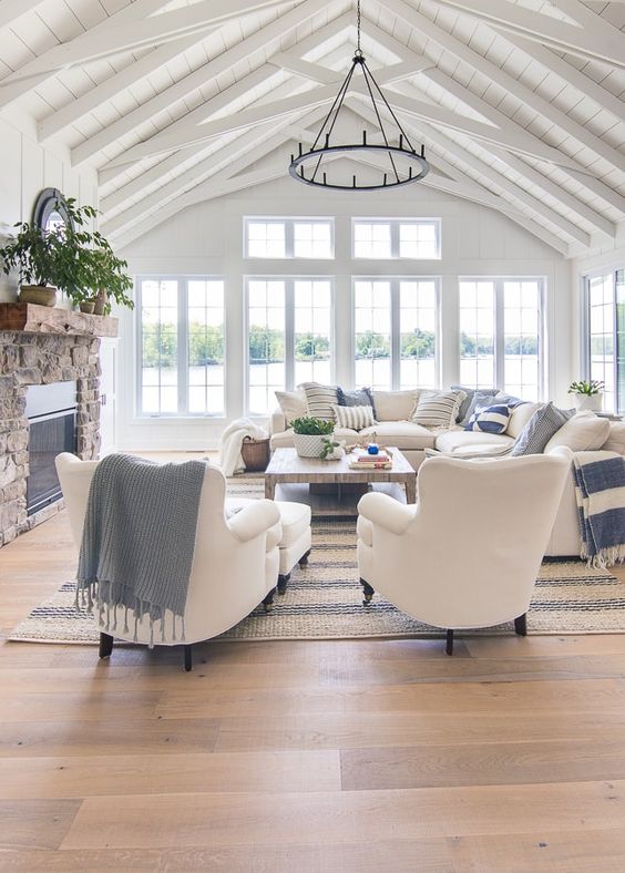 a beautiful coastal living room clad with white wood, with a stone fireplace, a low table and white furniture plus blue textiles
