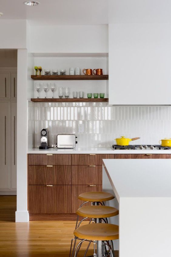 A mid century modern kitchen with stained and sleek white cabinets and a hood, a skinny tile backsplash and built in shelves