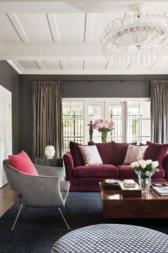 31 a refined living room with grey walls, a purple sofa, a grey chair, round and square coffee tables and a catchy crystal chandelier
