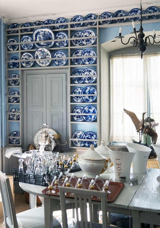 a refined dining space with light blue walls, built-in shelves with chinoiserie, neutral vintage furniture and a vintage chandelier