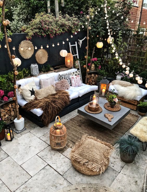 a boho backyard with candle lanterns, string lights and paper lamps over the space, potted blooms and greenery around