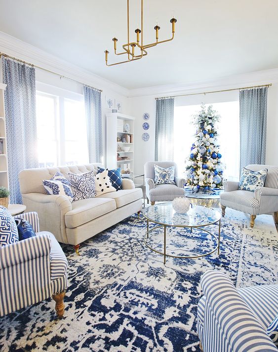 a glam blue and white living room with a white sofa and striped furniture, printed pillows and a rug, blue curtains and a gold chandelier
