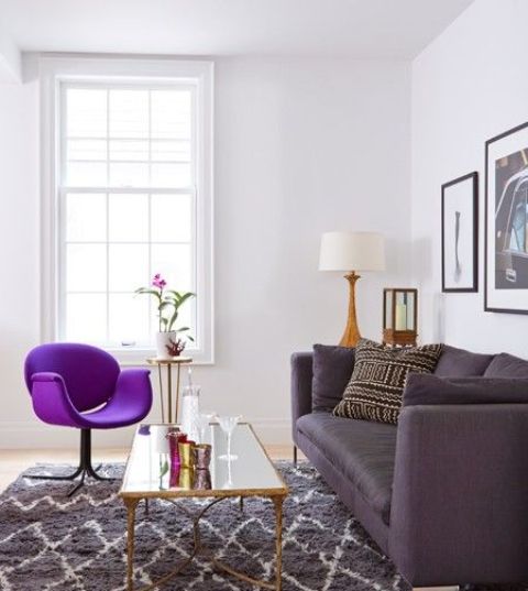 a stylish living room in neutrals, with a grey printed rug, a deep purple sofa, a bold purple chair, a chic gallery wall and a mirror table