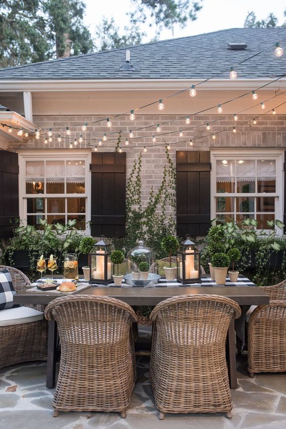 a stylish backyard dining space with a wooden table and rattan chairs and string lights over the space