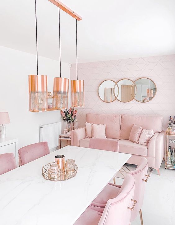 41 a chic dining room with a white stone table, pink chairs and a sofa, a blush accent wall, pendant lamps and round mirrors