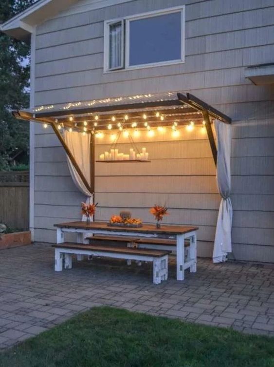 a backyard dining space with string lights over the space and a candle chandelier is a very cool and beautiful idea
