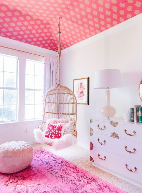 a glam space with a pink printed ceiling, a hot pink rug and pillow, a white dresser and an ottoman