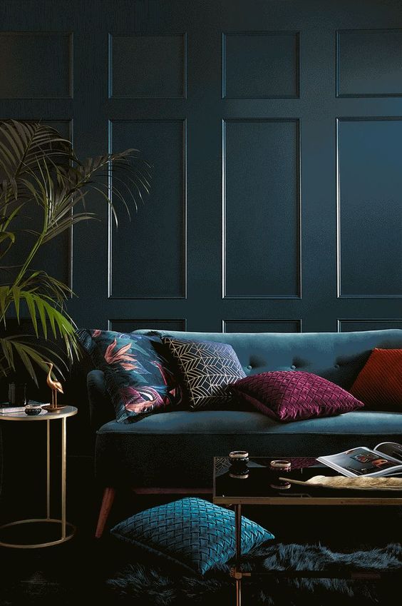 47 a modern and moody jewel tone living room with a teal panel wall, a teal sofa and pillows, a low table and potted plants