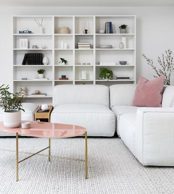 a Scandinavian living room with an open storage unit, a white low sofa, a pink coffee table and pink pillows