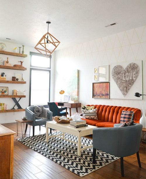 A beautiful mid century modern living room with floating shelves, an orange sofa, grey chairs, a low table and a geometric pendant lamp