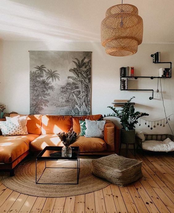 a boho living room with an orange sectional, a low table, a jute ottoman and a rug, a woven pendant lamp and potted plants