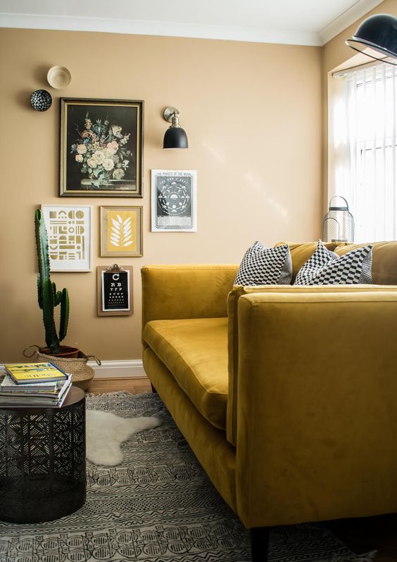 a boho nook with yellow walls, a mustard sofa, a gallery wlal and sconces and layered rugs plus a potted cactus