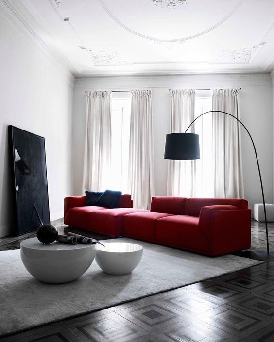 a bold contemporary living room with a large red sofa, a black artwork and a floor lamp and a duo of round tables