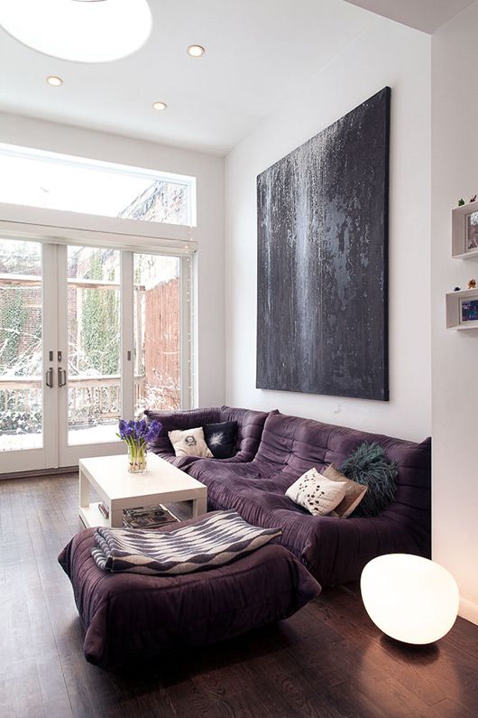 a bold modern living room with a low purple sofa and a large pouf, a white table and an oversized black artwork