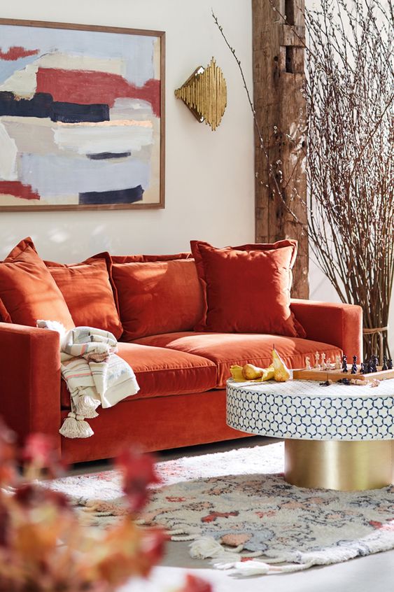 a bright living room with an orange sofa, a round table, a bold artwork and blooming branches arranged for decor