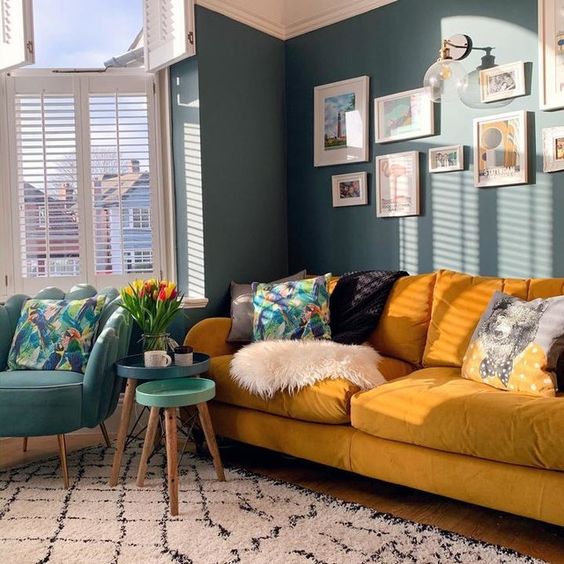 a bright living room with blue walls, a yellow sofa and printed pillows, a blue chair and round tables is chic and welcoming