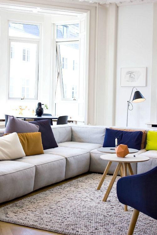 a bright modern living room with a grey low sofa, a bold blue chair, colorful pillows, some lamps and round tables