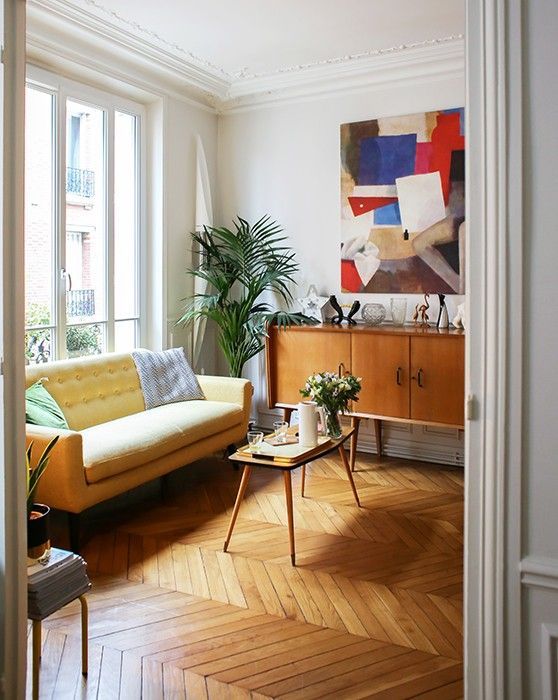 A bright modern living room with a light yellow sofa, a colorful artwork, mid century modern furniture and greenery