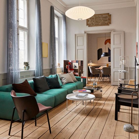 a catchy living room with a low emerald sofa, roudn tables, various chairs, lamps and artworks is chic