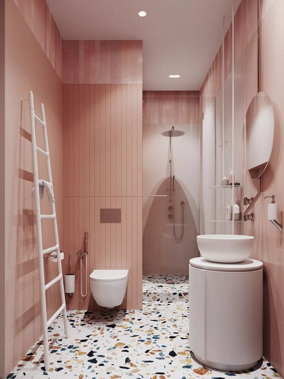 a catchy rose bathroom with pink walls, a colroful terrazzo floor, a roudn vanity and a round sink and a ladder