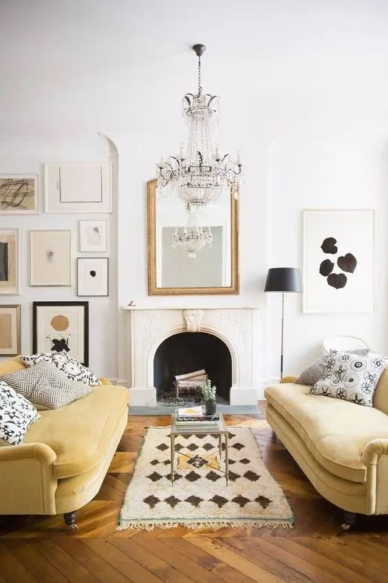 a chic living room with a non-working fireplace, a monochromatic gallery wall, a crystal chandelier and a duo of light yellow sofas