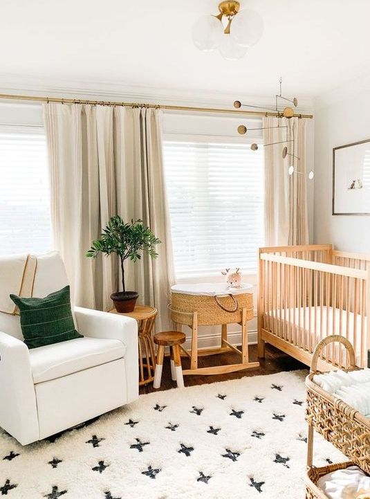 a chic modern nursery with a printed rug, a white chair, a wooden crib and a rattan cart for storage, green touches