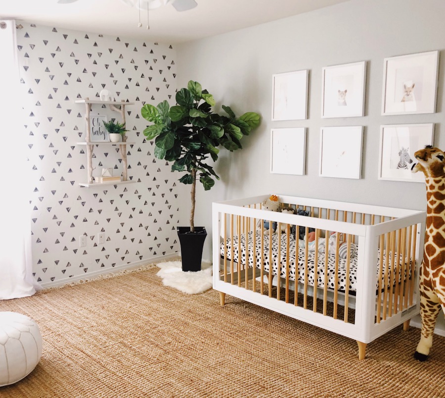 a chic neutral nursery with a geo print wall, a crib with leopard bedding, a chic gallery wall and a potted plant in the corner