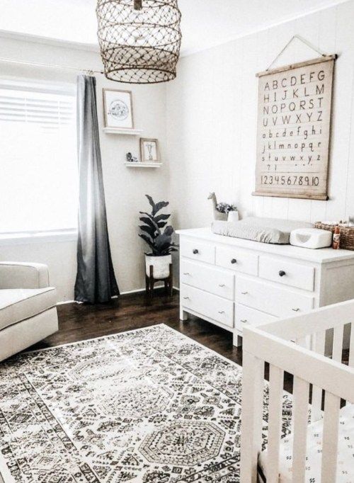 a chic neutral nursery with white furniture, a printed rug, grey curtains, a functional artwork, some shelves with art