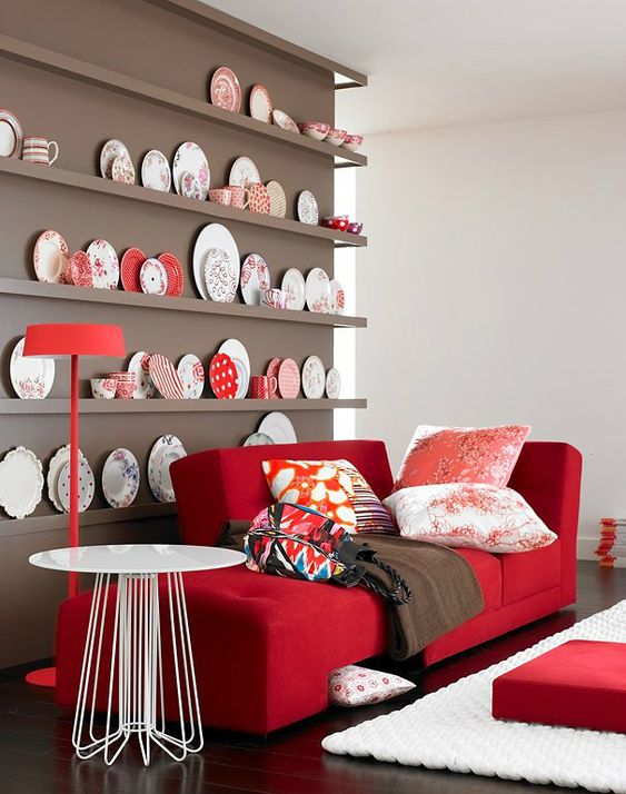 a chic nook with a taupe wall and a collection of decorative plates, a red couch and printed pillows plus a round table