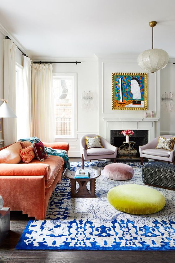 a colorful eclectic living room with a fireplace, lilac chairs, an orange sofa, Moroccan furniture, a rug and poufs is bold