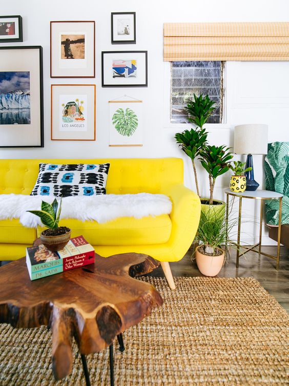 a colorful living room with a neon yellow sofa, a bright gallery wlal, potted plants and a wood slice coffee table