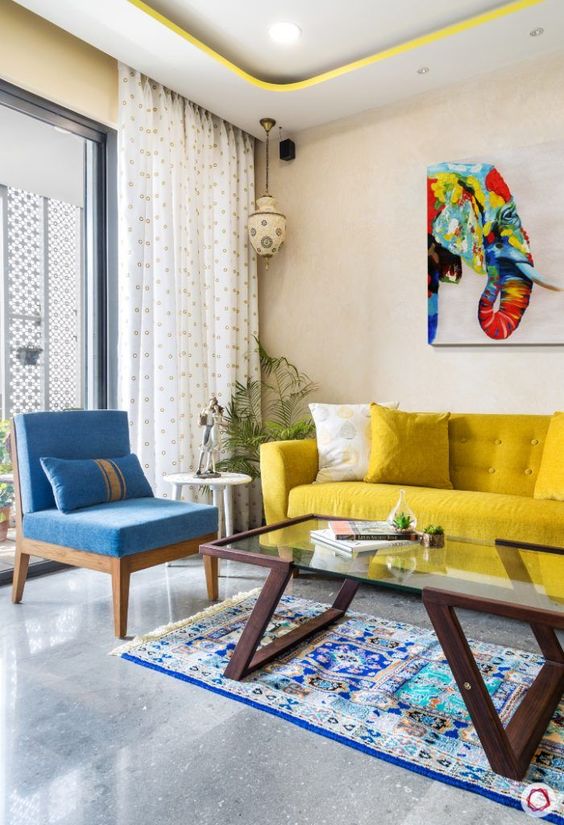 a colorful living room with neutral walls, a yellow sofa, a blue chair, a glass table and a colorful artwork is amazing