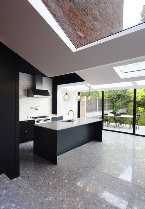 a contemporary kitchen with black cabinetry, a black kitchen island and white tiles and a grey terrazzo floor that adds eye-catchiness