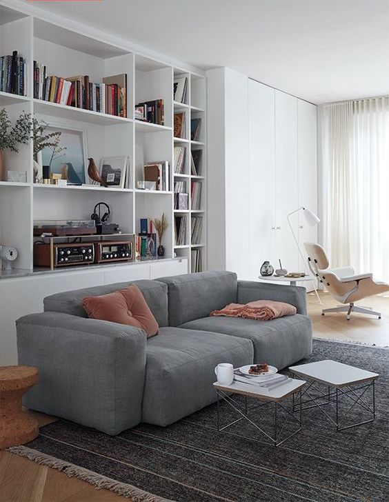 a contemporary living room with built-in storage units, a grey low sofa, a couple of coffee tables and a white lounger