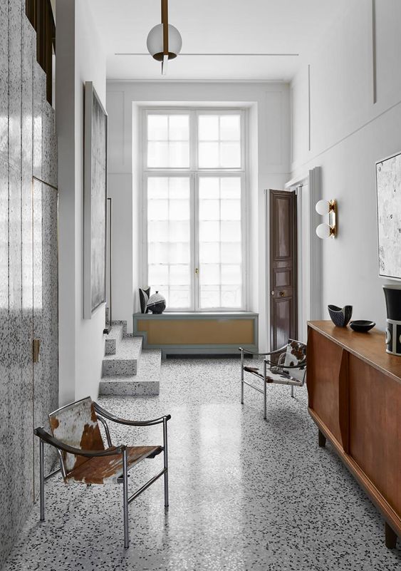 A cool mid century modern entryway with a terrazzo floor and a wlal, leather and metal chairs and a chic wooden credenza