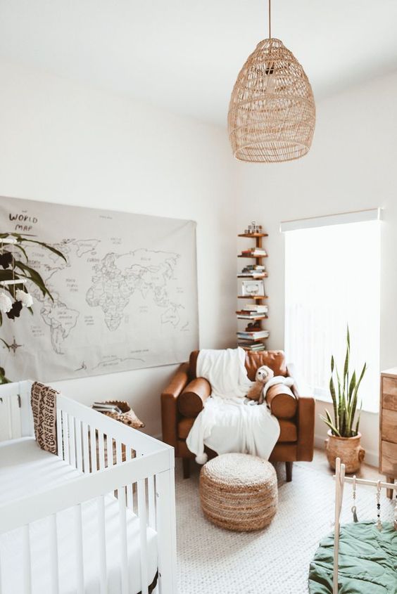 a cool neutral nursery with a white crib, a brown chair, a stained shelf in the corner, a woven lamp and a map of the world