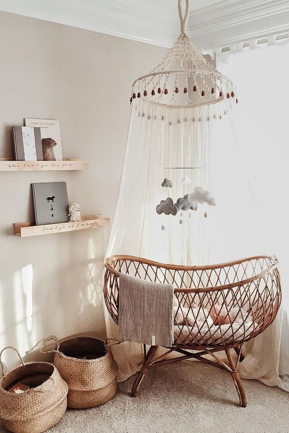 a cool neutral nursery with floating shelves, a rattan crib, a canopy and a mobile and baskets for storage