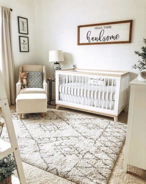 a cozy neutral nursery with a modern crib, a cozy chair with a footrest, some artworks and pretty neutral textiles