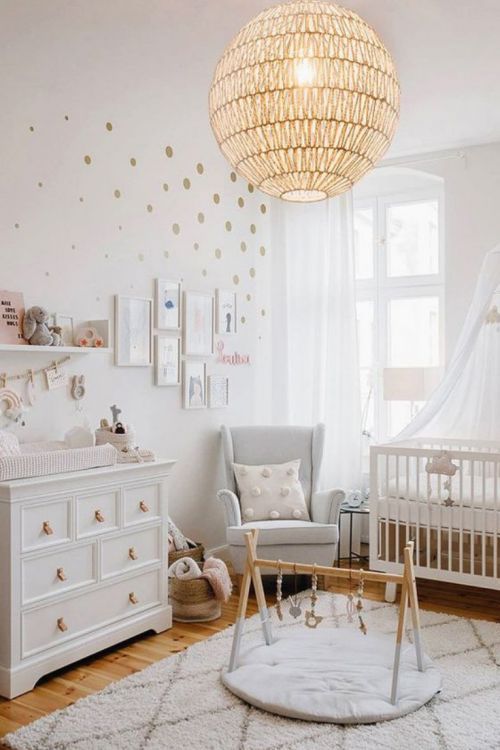 a cute and lovely neutral nursery with white and grey furniture, layered rugs, a sphere lamp and polka dot touches