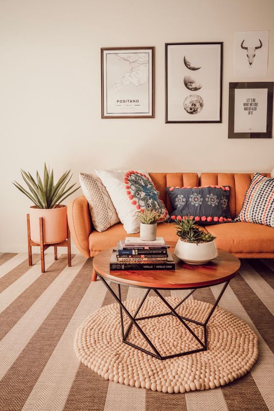 a lovely boho living room with an orange leather sofa, a wooden bead rug and a geo table, a monochromatic gallery wall