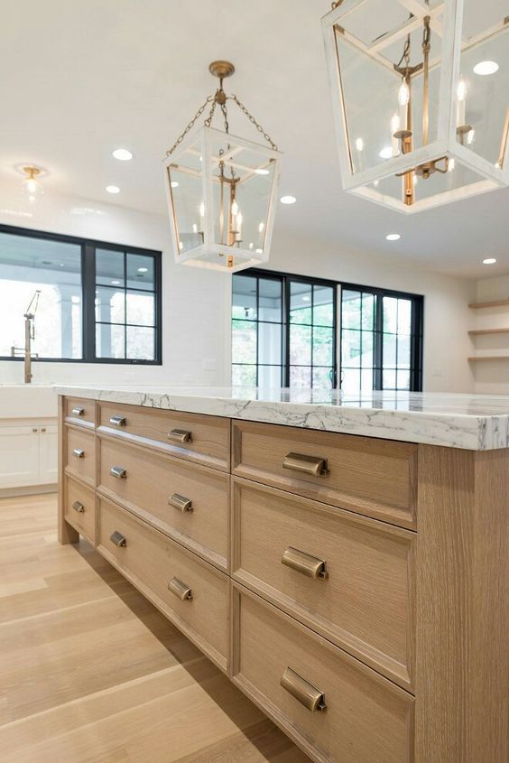 a lovely kitchen with a blonde wood floor and a large kitchen island with storage, elegant faceted pendant lamps