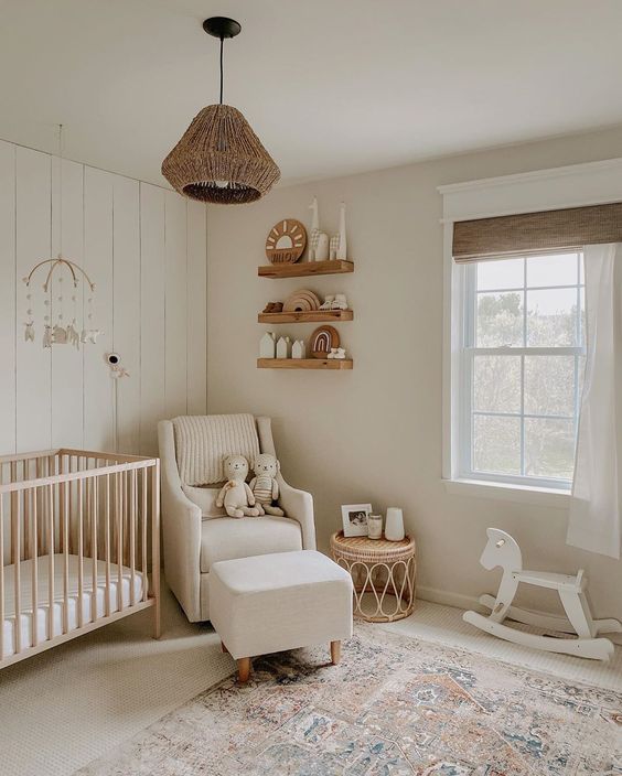 a lovely modern neutral nursery with floating shelves, a light stained crib, a white chair and a footrest, a rattan pendant lamp and a printed rug
