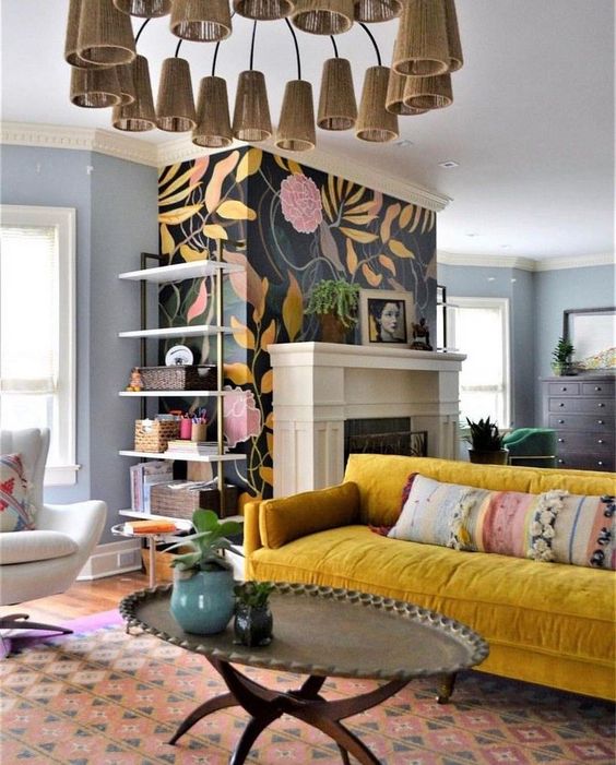 a maximalist living room with a fireplace, a floral wall, a msutard sofa, a low metal table and a cone chandelier