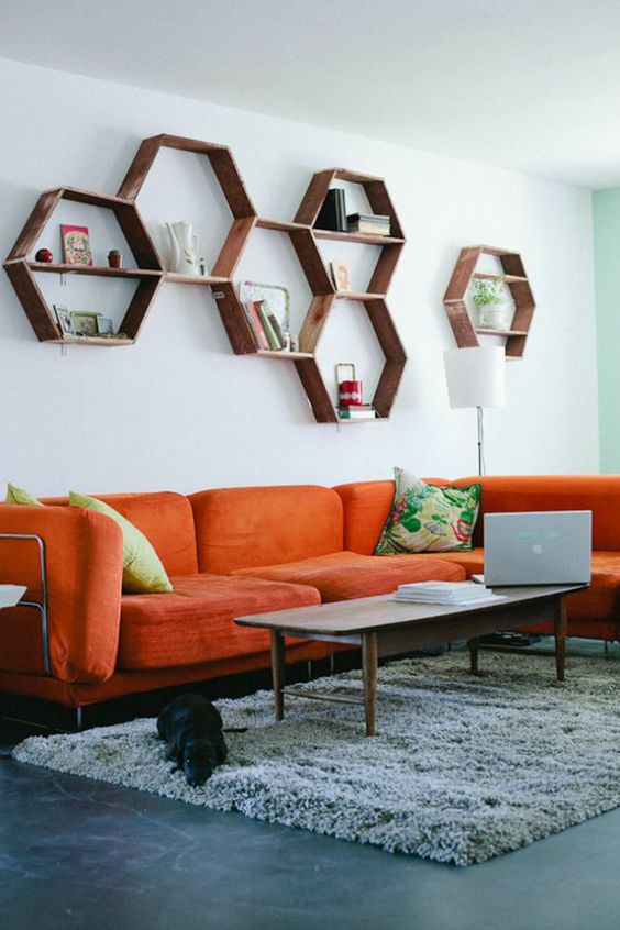 A mid century modern living room with an orange sofa, hexagon shelves, a low table and colorful pillows is welcoming