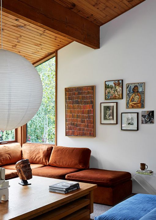 a mid-century modern space with a large rust-colored sectional, a low wooden table and a blue pouf plus a whimsy gallery wall