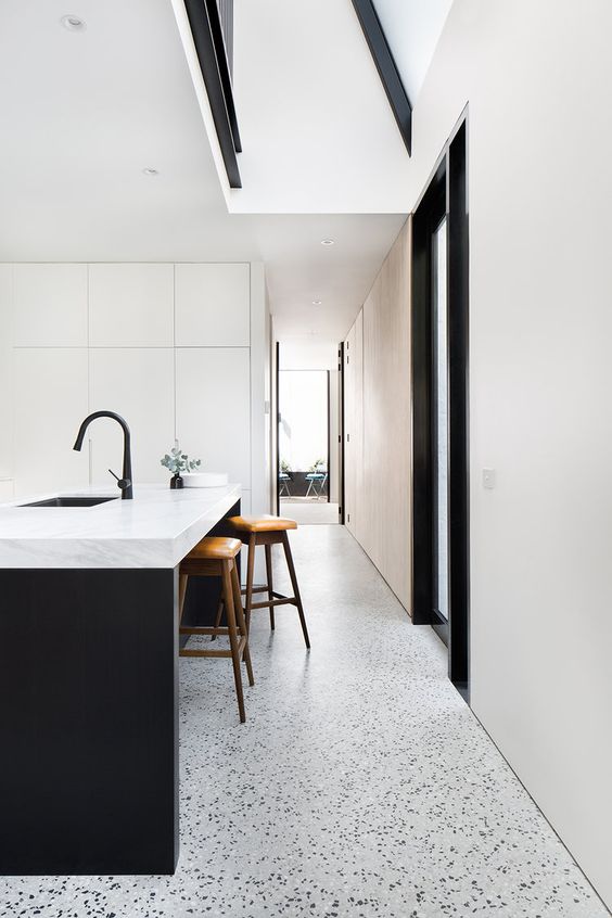 a minimalist kitchen with sleek white cabinetry, a black kitchen island, terrazzo floors and black fixtures