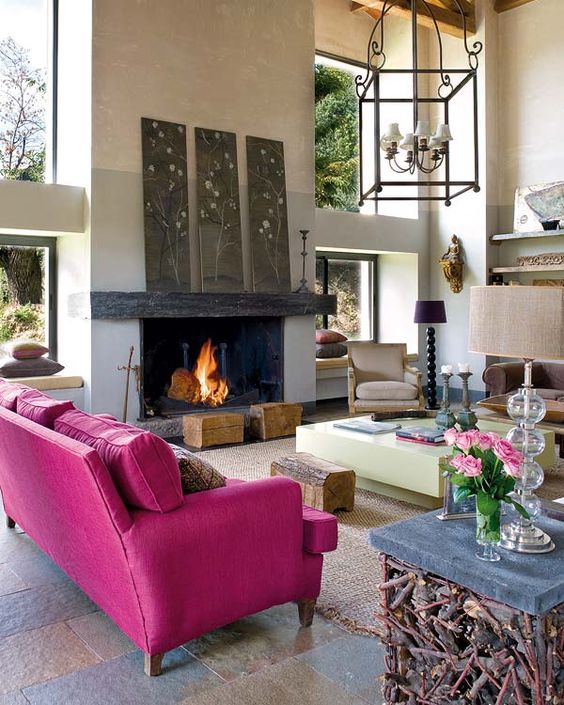 a modern living room with a fireplace, a hot pink sofa, floral artworks, a creative table with wood, tree stumps and catchy lamps